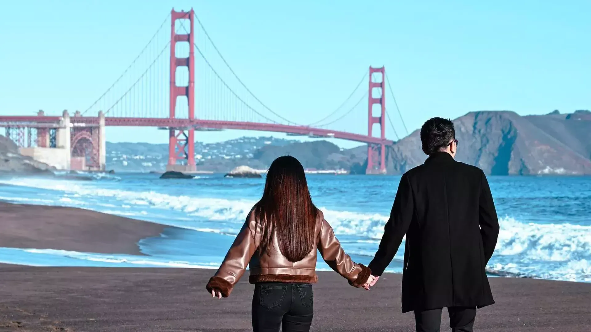 Couple holding hands at 贝克海滩 with Golden Gate bridge in background 