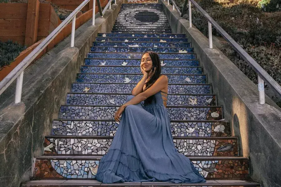 한 여성이 샌프란시스코 선셋 지역 16번가 타일 계단에 앉아 포즈를 취하고 있습니다.