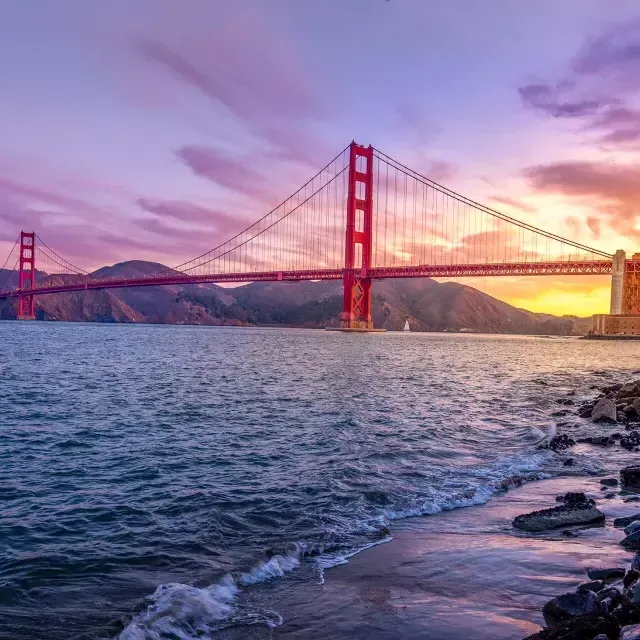 Die Golden Gate Bridge bei Sonnenuntergang mit einem bunten Himmel und der San Francisco Bay im Vordergrund.